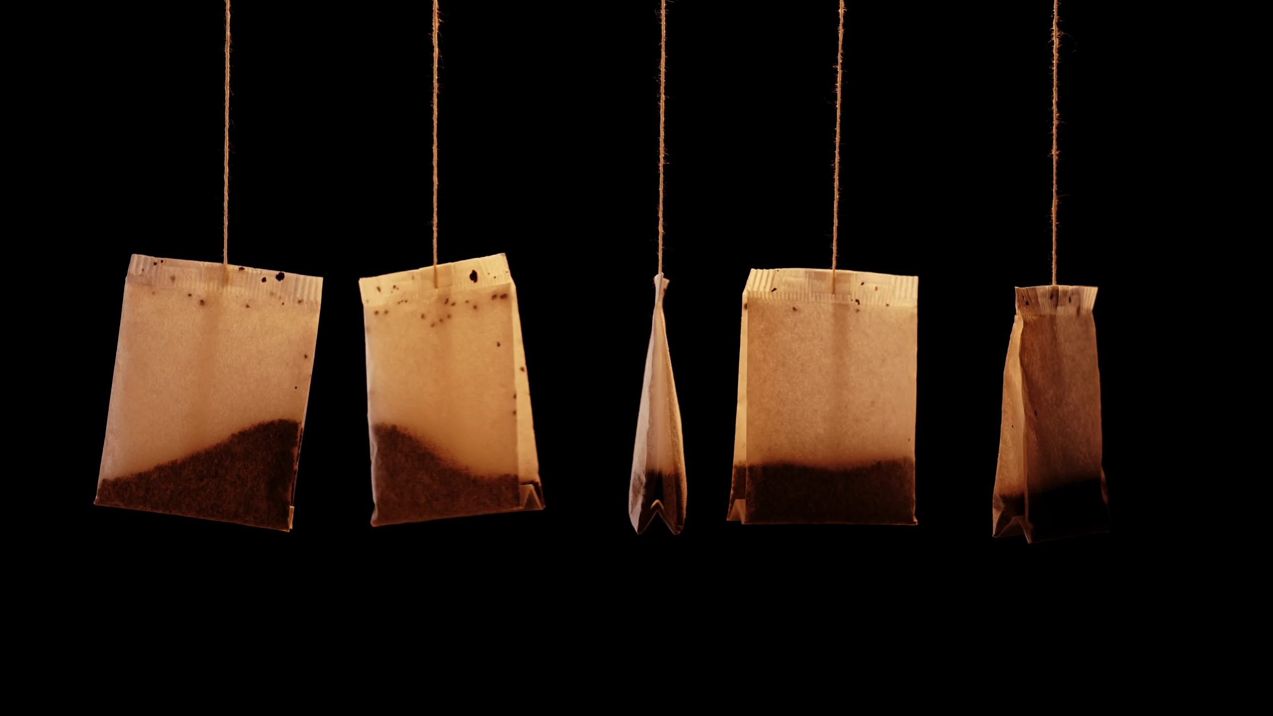 Used brown teabags with herbal brew hang on black background