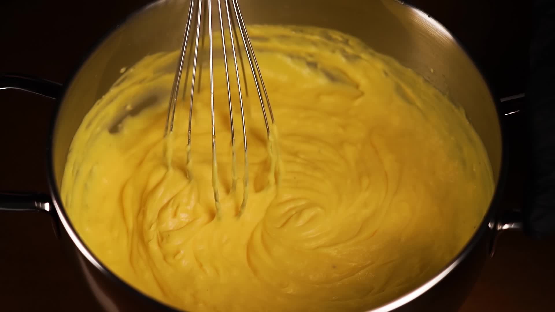 Impasto di miscelazione con frusta di metallo in casseruola sul primo piano nero