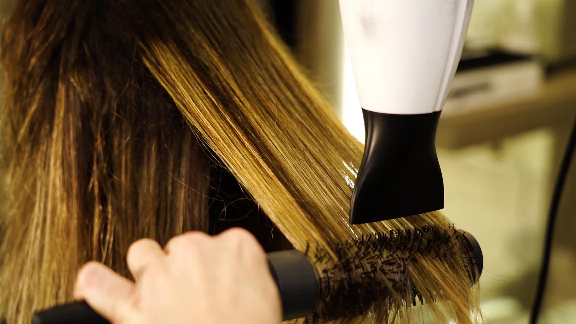 Hair dryer and brush straighten woman’s hair