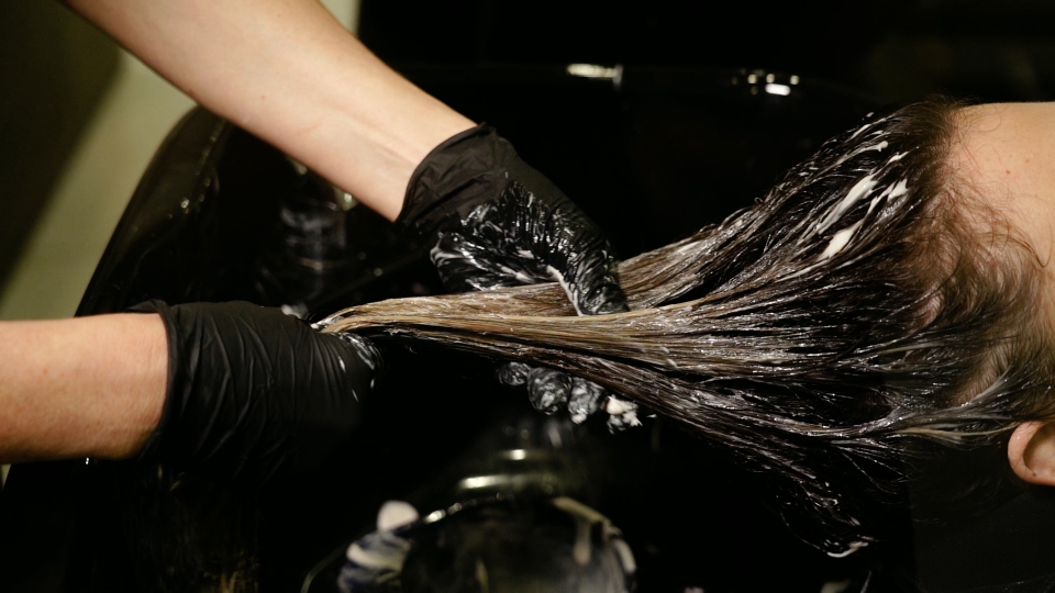 Woman in black gloves spreads lotion on lady long hair