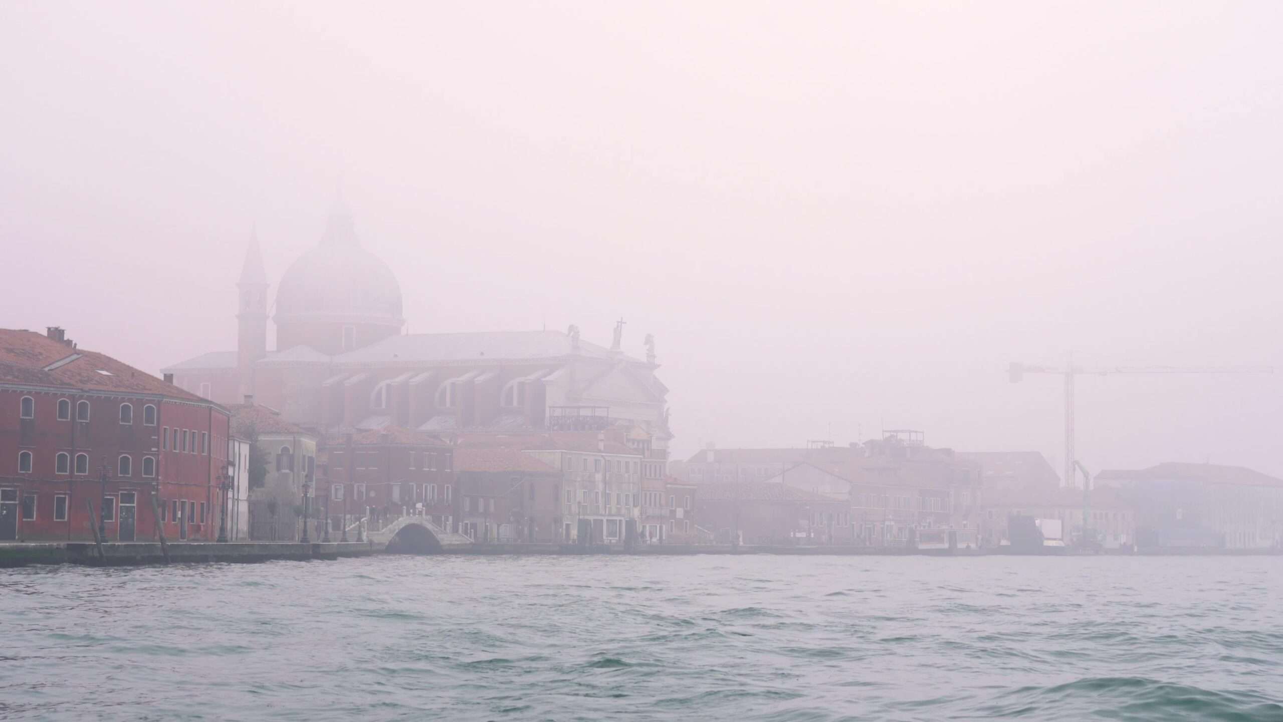 Gli edifici italiani si trovano in una fitta nebbia vicino all’acqua blu della laguna