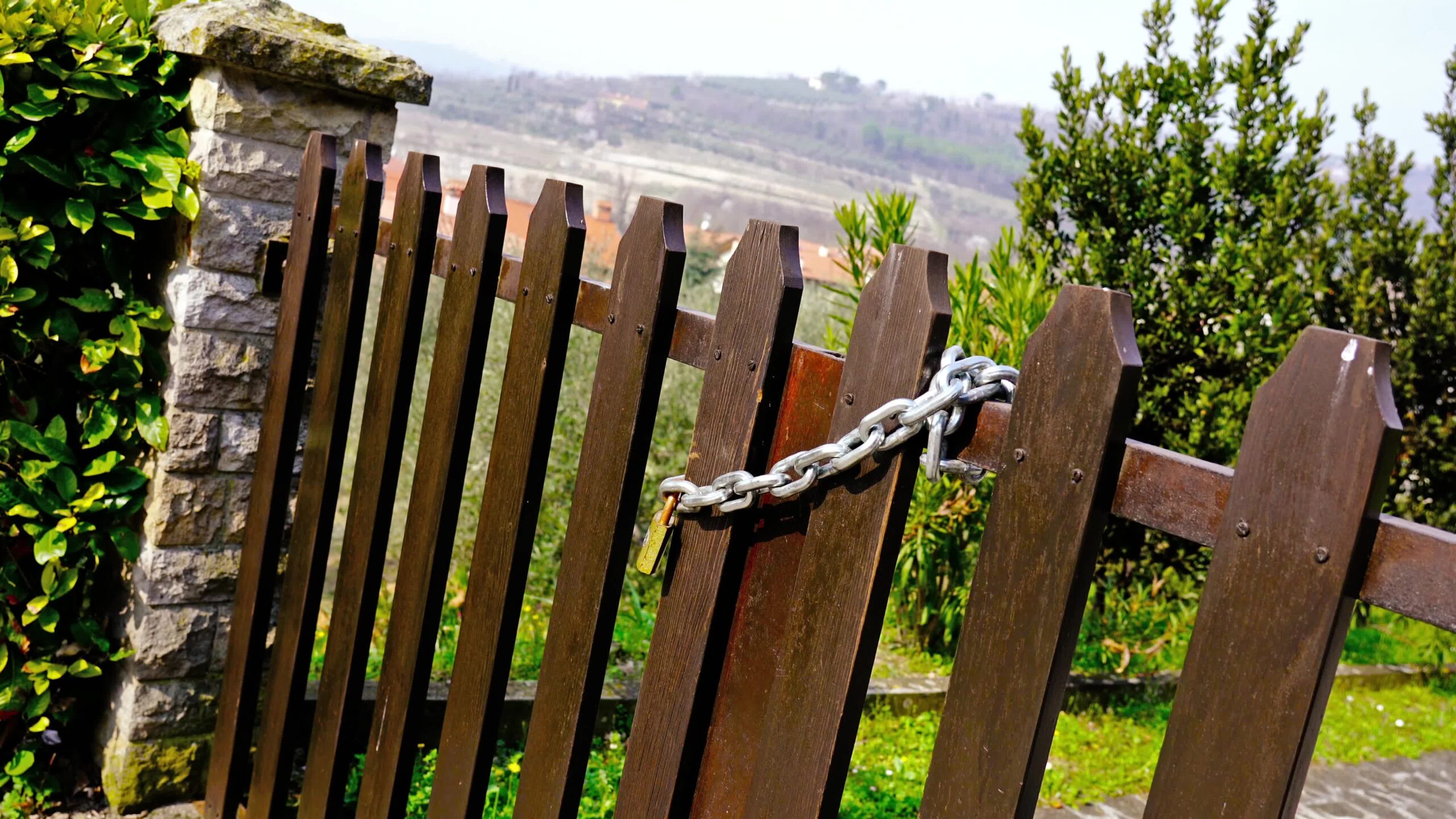 Silver metal chain hangs on brown wooden fence with stone