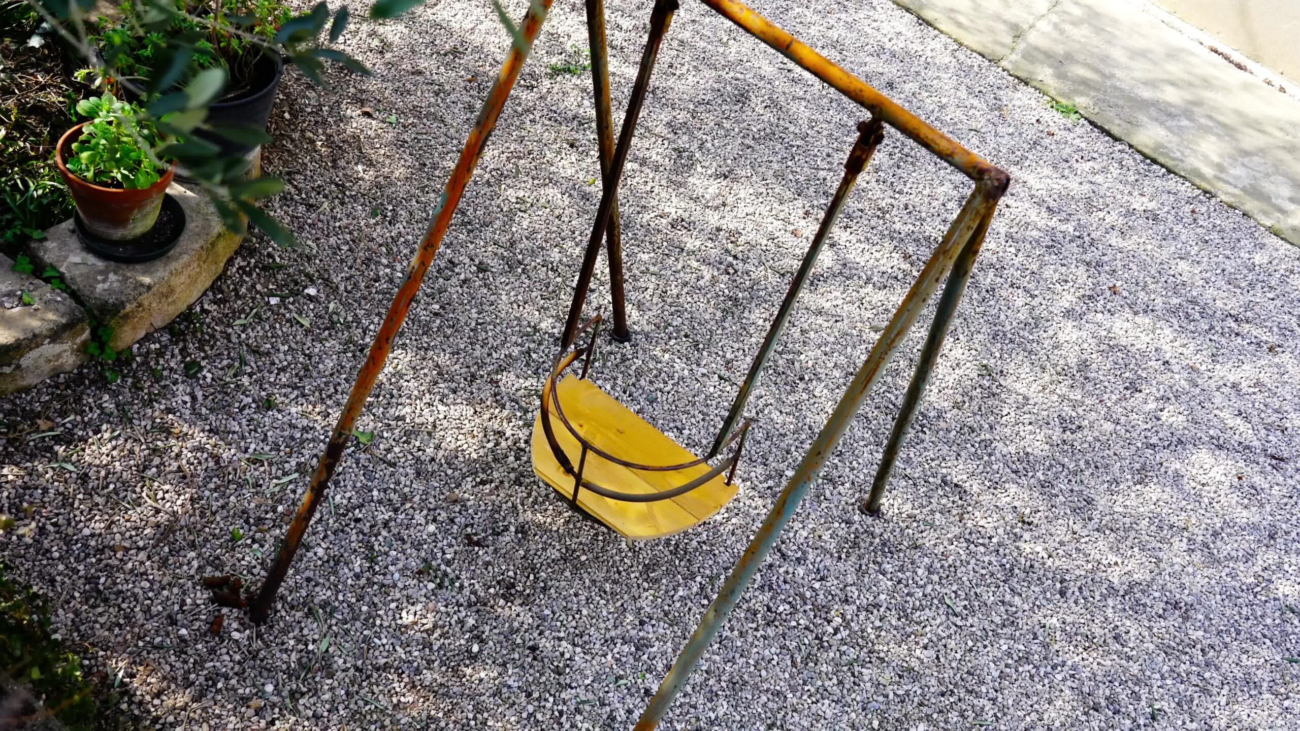 Small yellow swing with rusty elements stands in yard