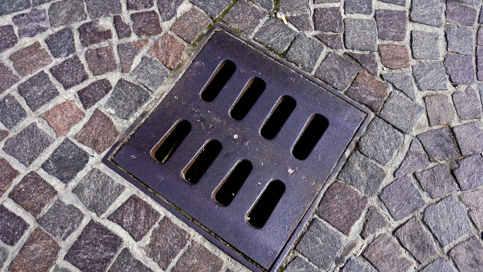 Small grey metal drain with holes mounted on paved road