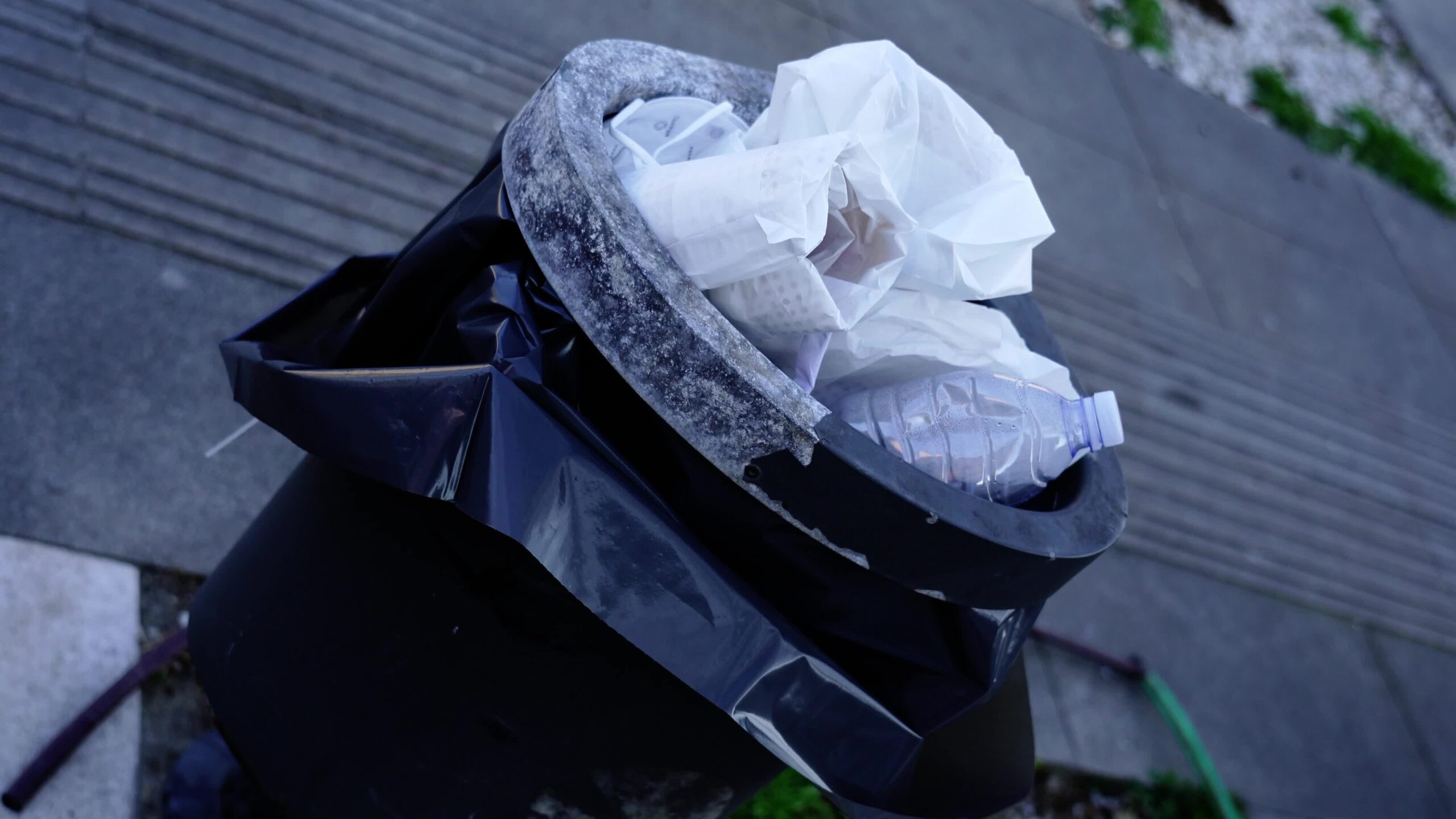 Filled black rubbish bin with black plastic bag and litter