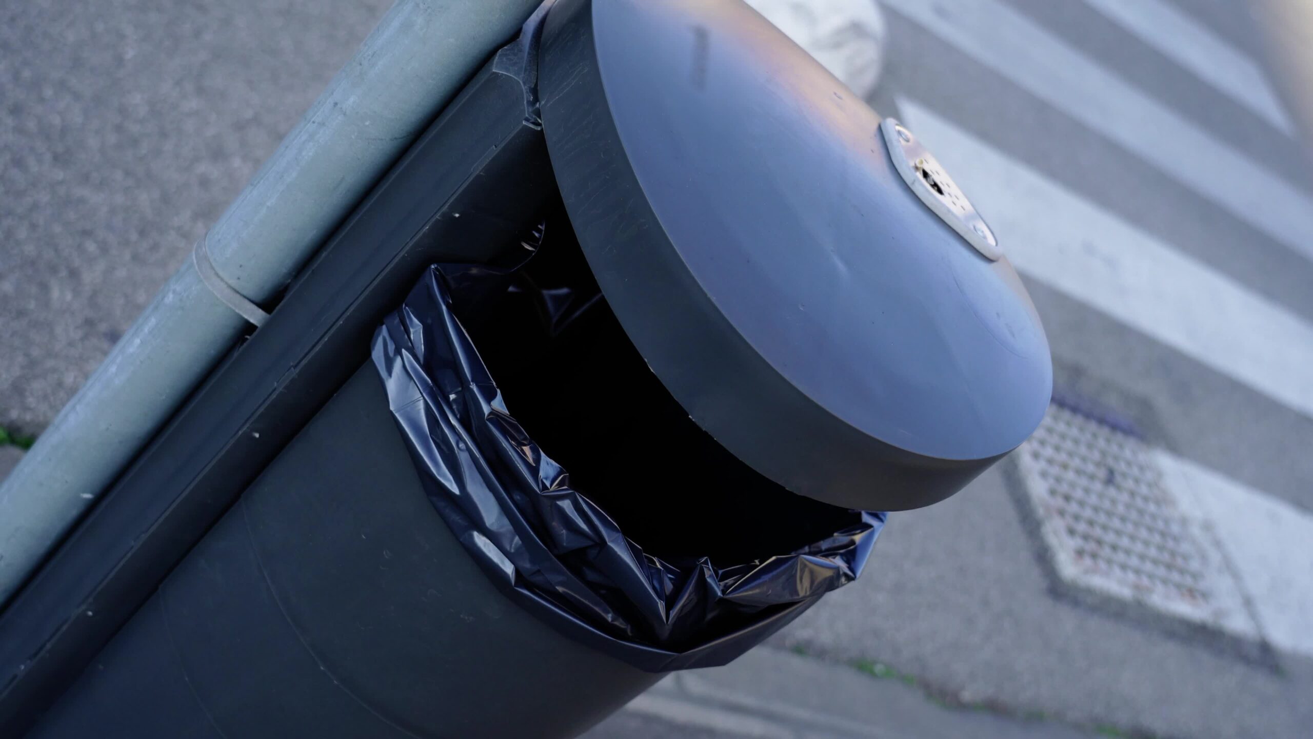 Black rubbish bin fixed on grey streetlight pole near road