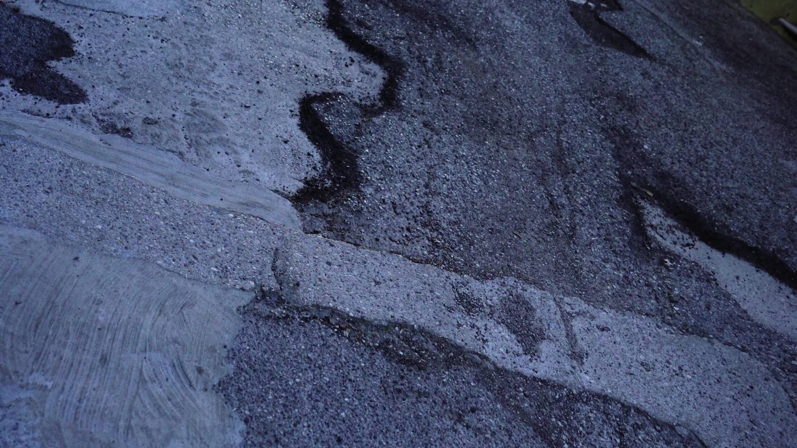 Strada asfaltata grigia bagnata con piccole buche e linee nere