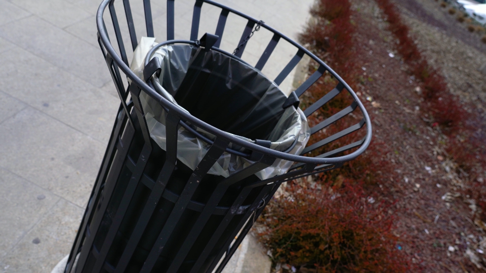 Cylinder metal rubbish bin on paved path near green bushes