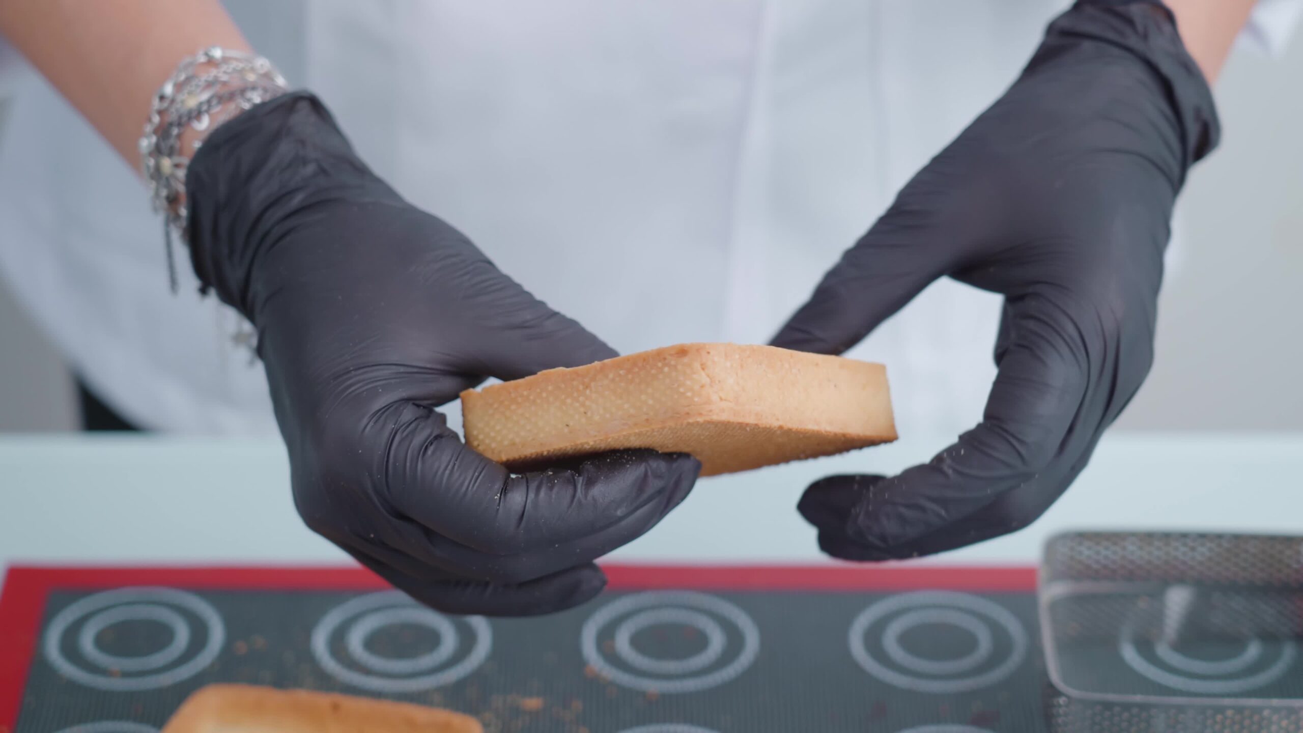 La persona in guanti da lavoro neri mostra la filatura di biscotti nelle mani