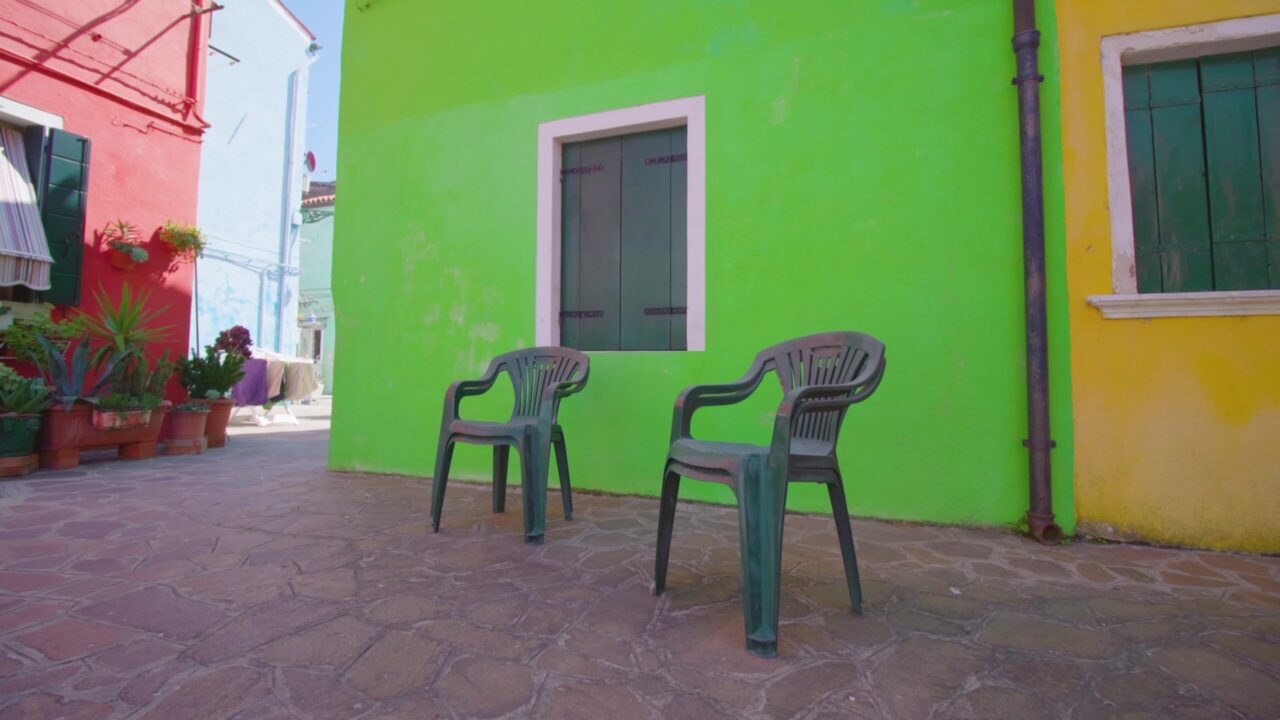 Street with plastic chairs standing in shadow yard in Burano