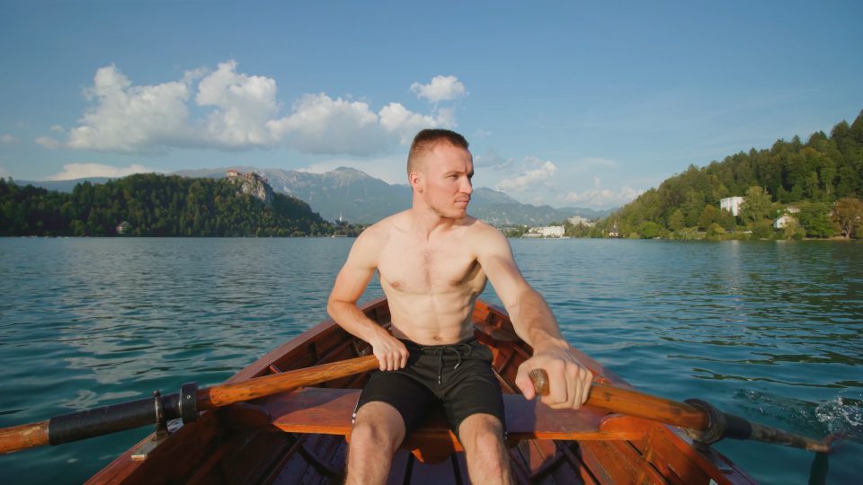 Young man controls paddles in wooden boat on Bled lake