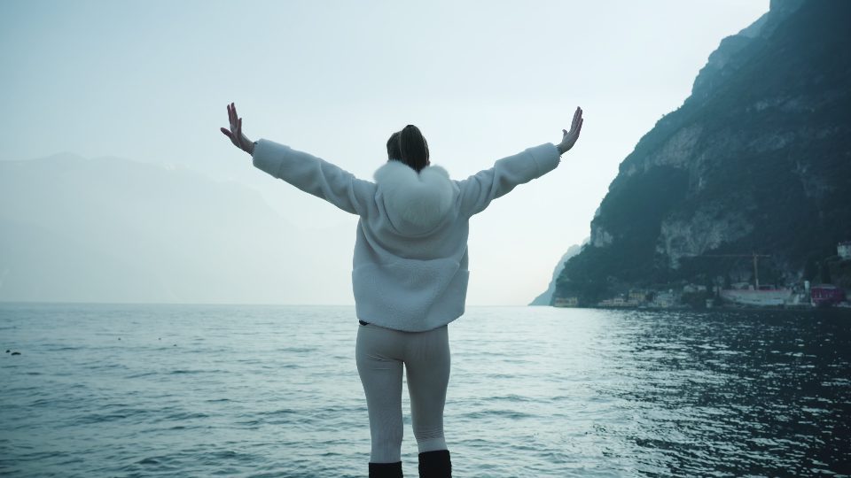 Woman raises hands against shimmering water in lake Garda