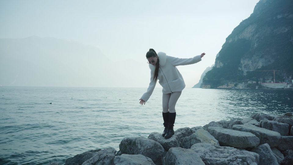 Woman steps on big stones on bank of lake Garda in Italy