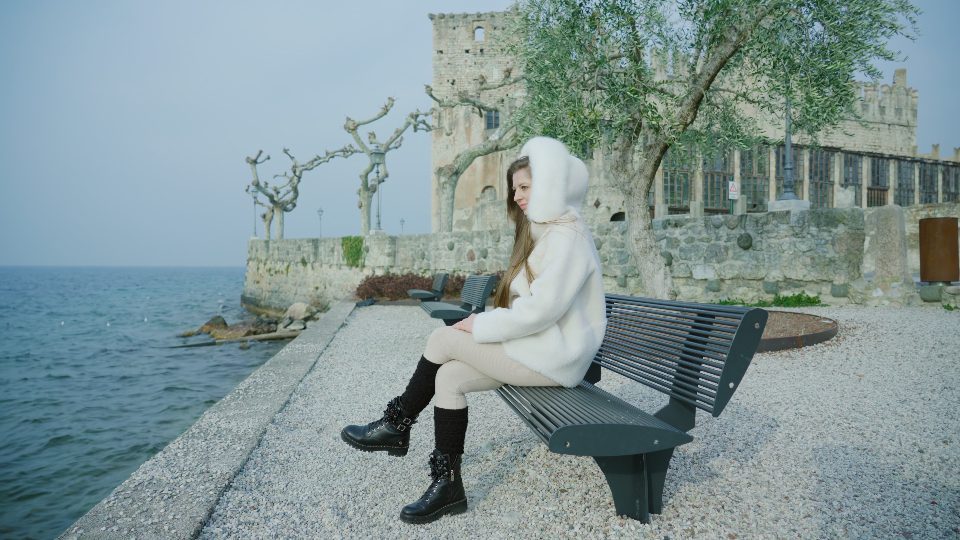Woman sits on bench against ancient building looking at lake