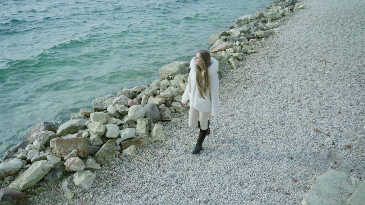Woman walks on pebbled bank near rocks looking at lake