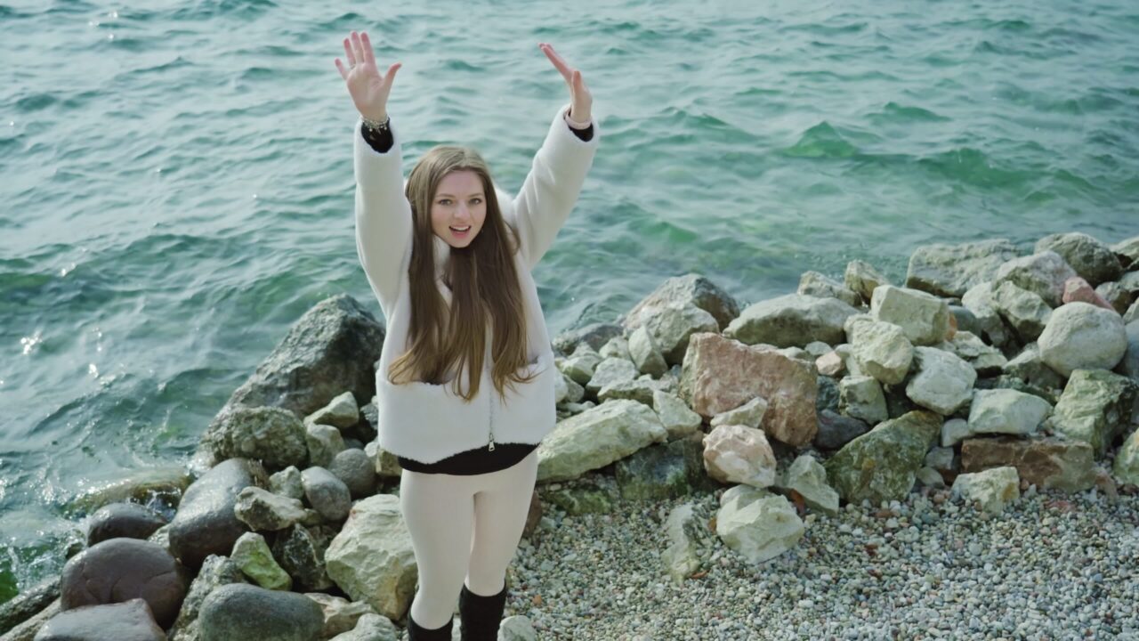 Happy woman raises hands catching wind on bank of lake