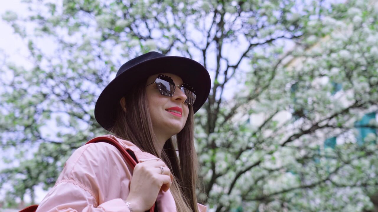 Woman in hat stands against blooming tree looking around