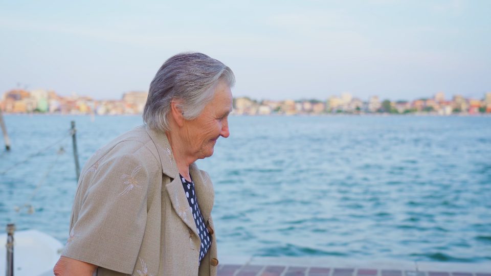 Elderly lady traveler walks on promenade in Chioggia smiling