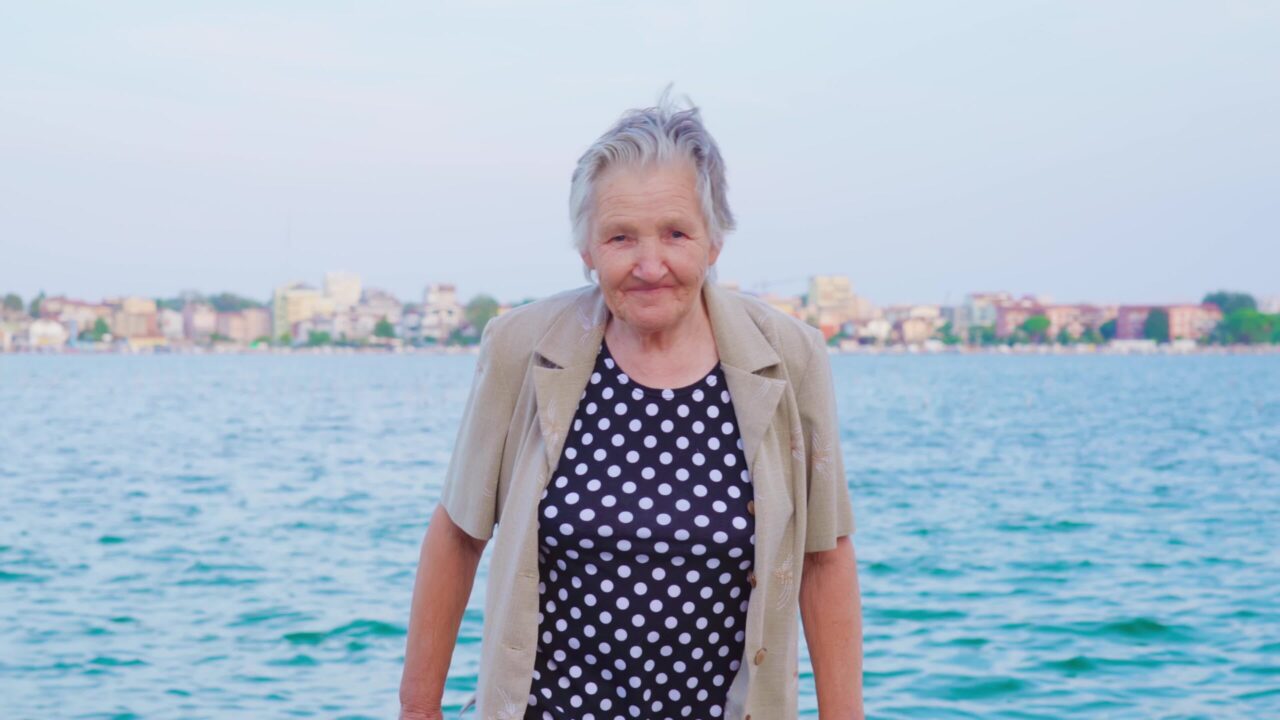 Donna anziana passeggia in riva al mare sorridendo ampiamente