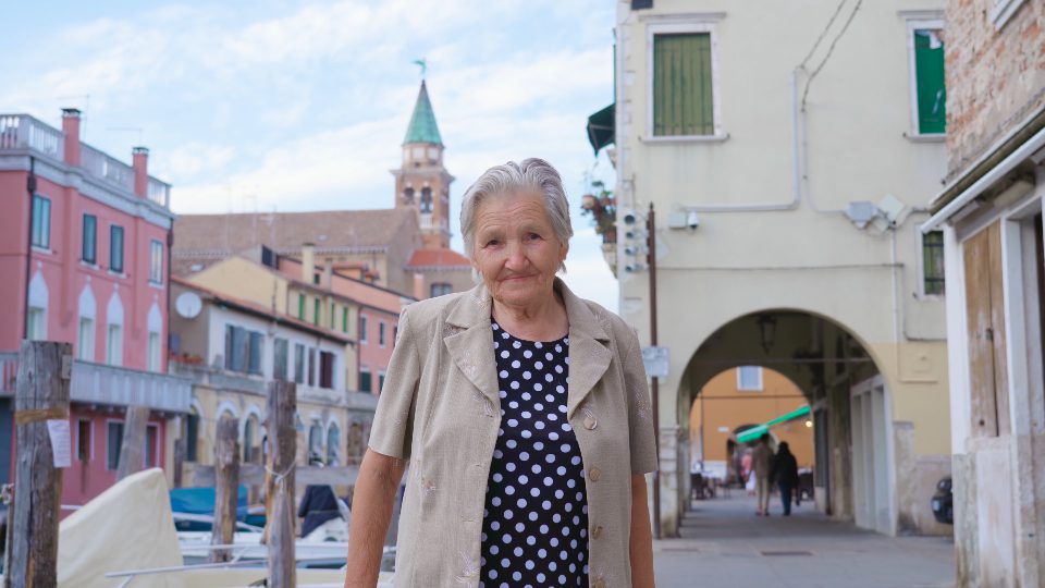 Old woman stands on channel embankment street with houses