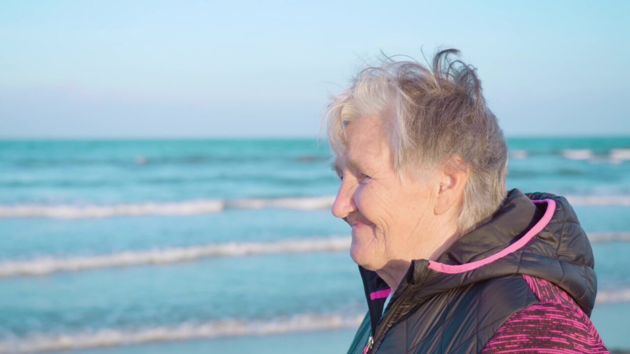 Old woman with hair waved by wind enjoys sea view on coast