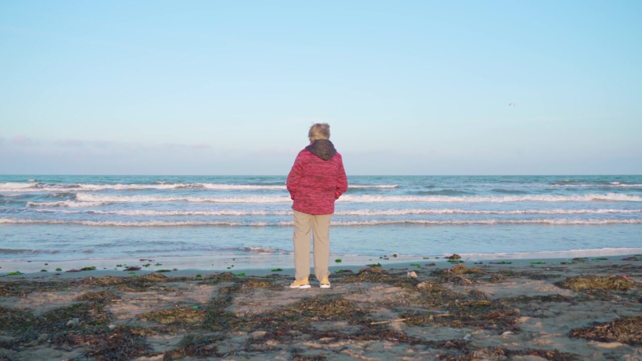 Woman looks at rolling sea waves standing on wet beach