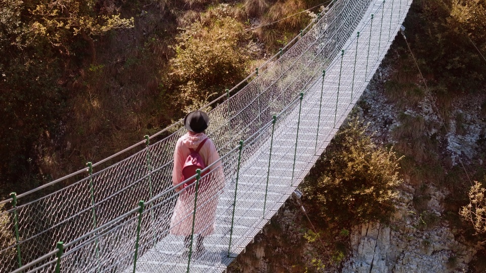 Woman walks on suspension footbridge enjoying autumn views