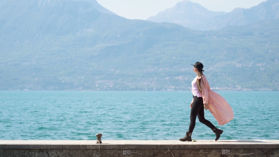 Woman walks on pier at lake Garda against giant mountains