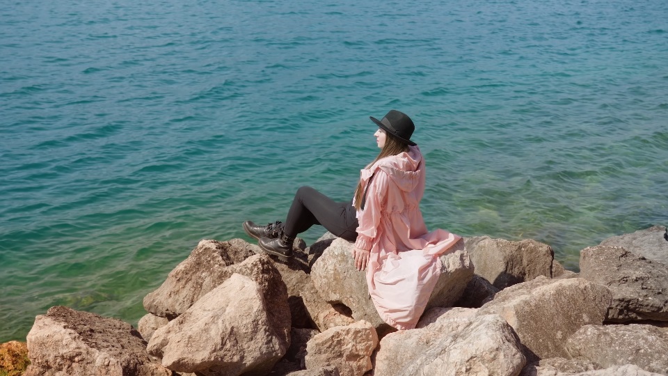 La donna si siede sulle pietre che esaminano l’acqua luccicante del lago