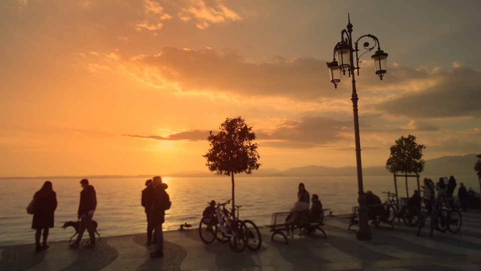 People watch beautiful sunset on city embankment near lake