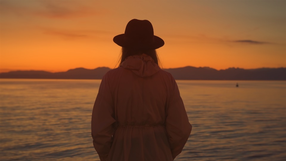 Woman in dark hat watches bright sunset at Lake Garda