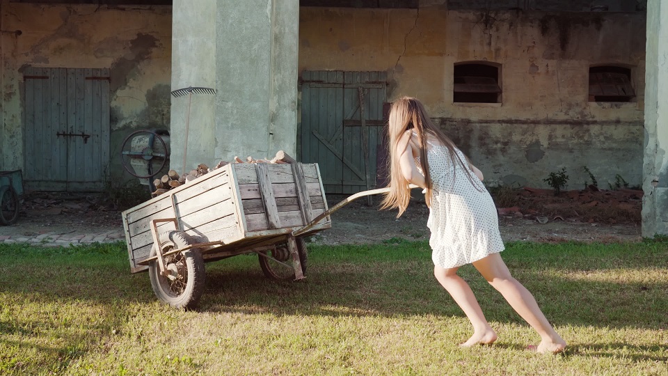 Long-haired woman pushes heavy wooden cart with firewood