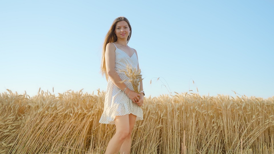 Long-haired woman stands in golden field holding bouquet