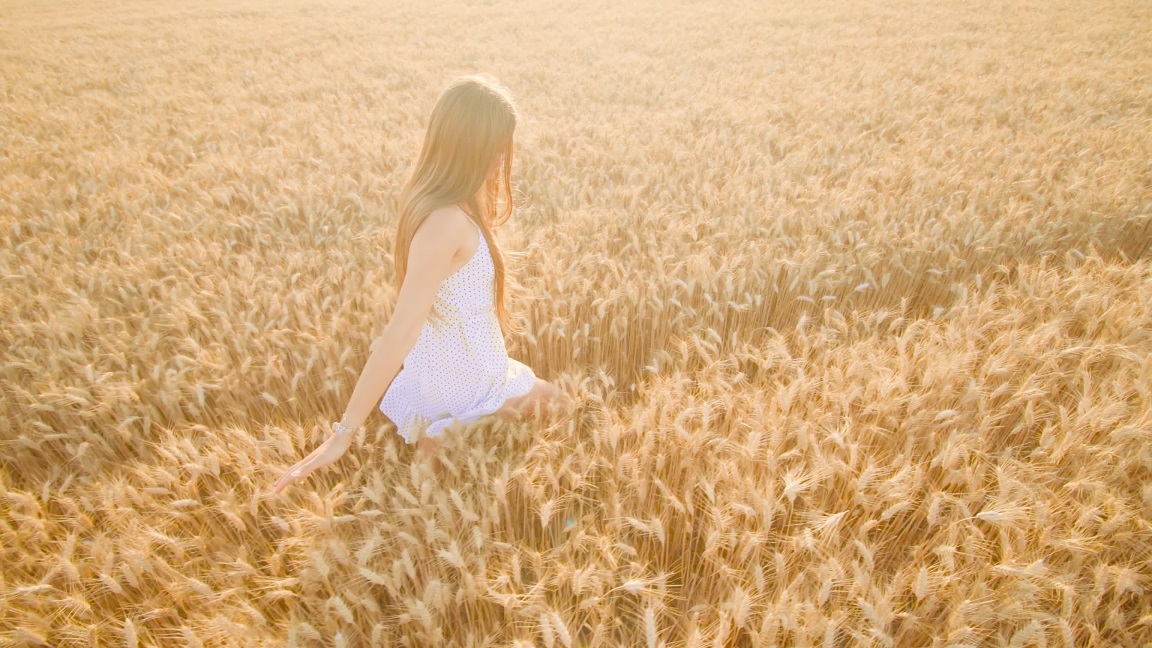 Young woman walks in ripe wheat field touching spikelets