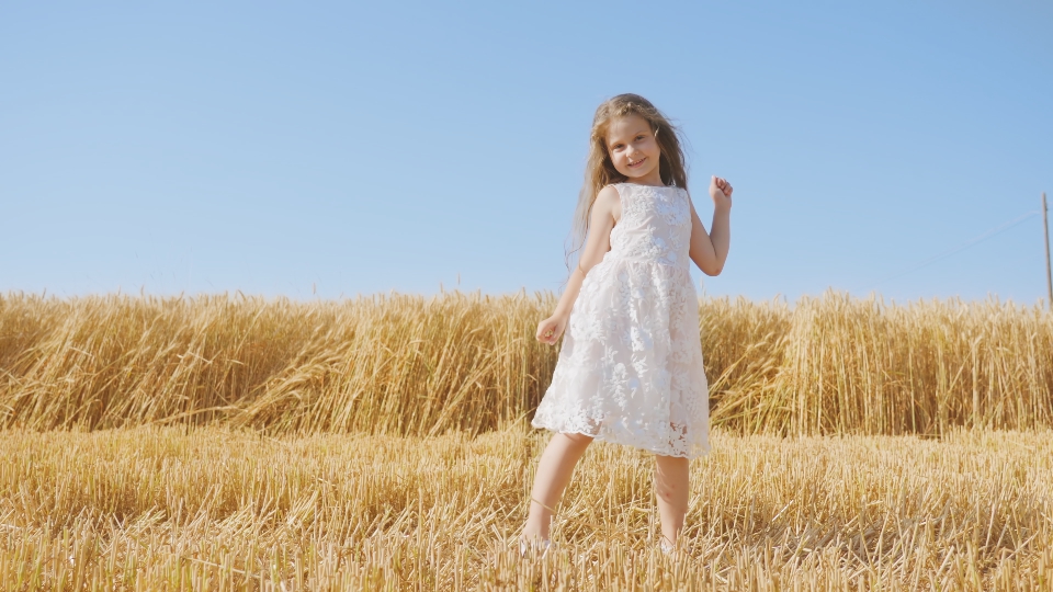 Long-haired girl dances in golden wheat field on sunny day