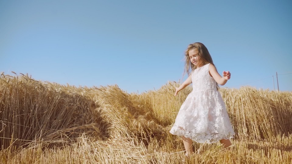 Smiling girl in white dress walks in golden wheat field