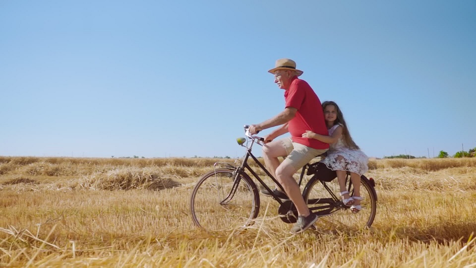 La ragazza bionda ama andare in bicicletta con il nonno sul campo di grano