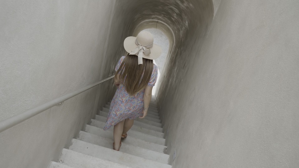 La donna con il cappello scende le scale camminando verso l’uscita del corridoio