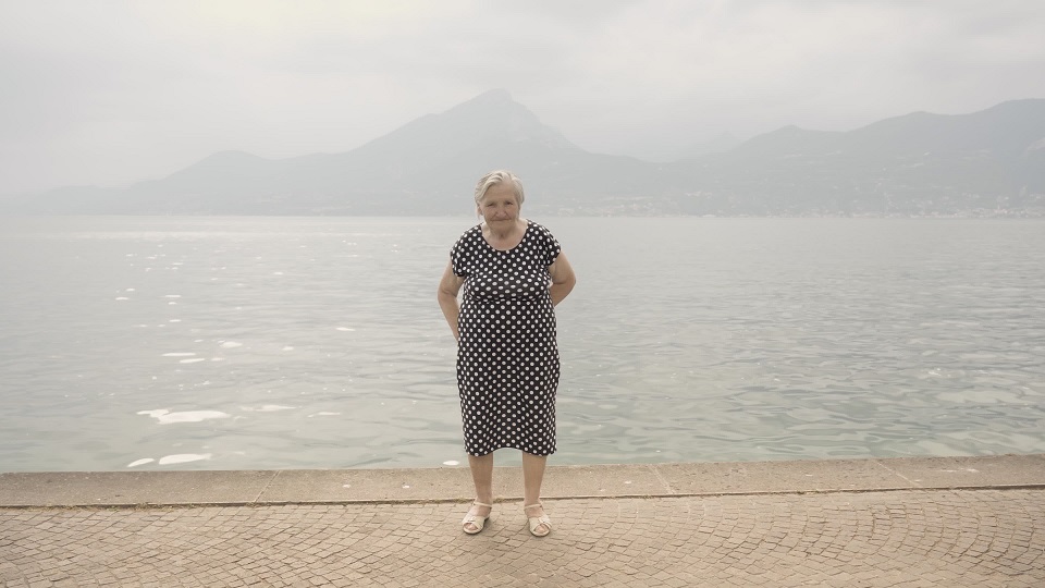 Senior woman in polka-dot dress stands on embankment