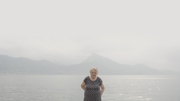 Senior donna si erge contro il Lago di Garda guardando a porte chiuse