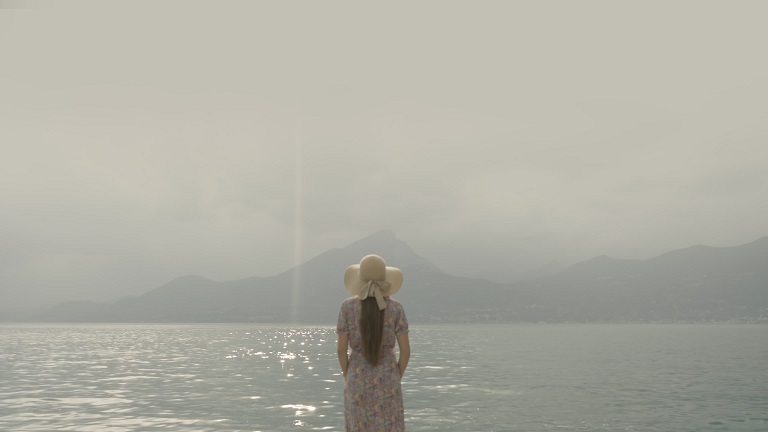 Woman stands against Lake Garda with shimmering water