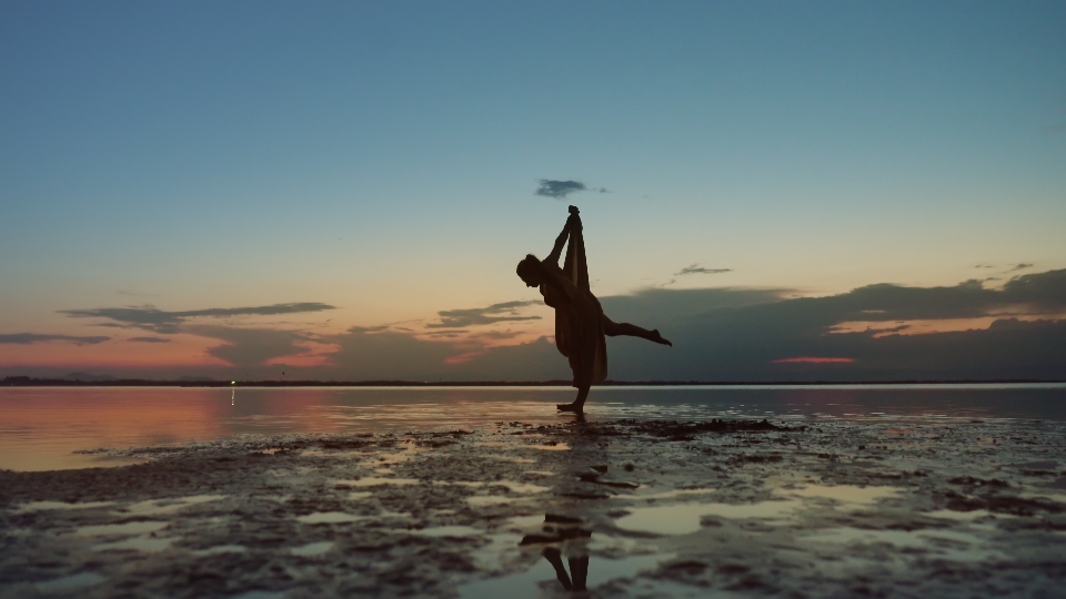 Ballerina cerca di mettersi su un agamba sull aspiaggia al tramonto