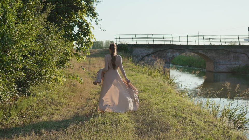 Donna in abito elegante cammina a piedi nudi con i tacchi in mano in campagna