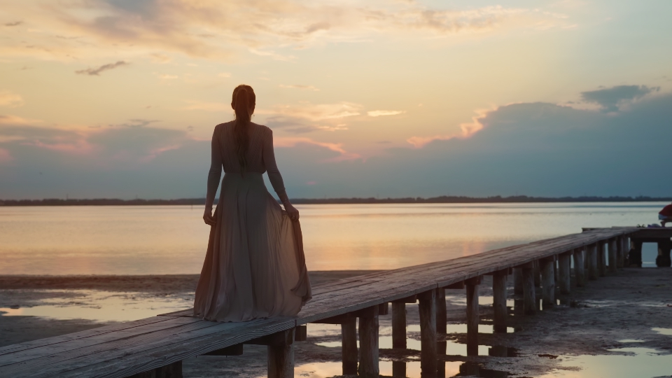 Donna cammina di spalle sulla passeggiata in legno della laguna al tramonto