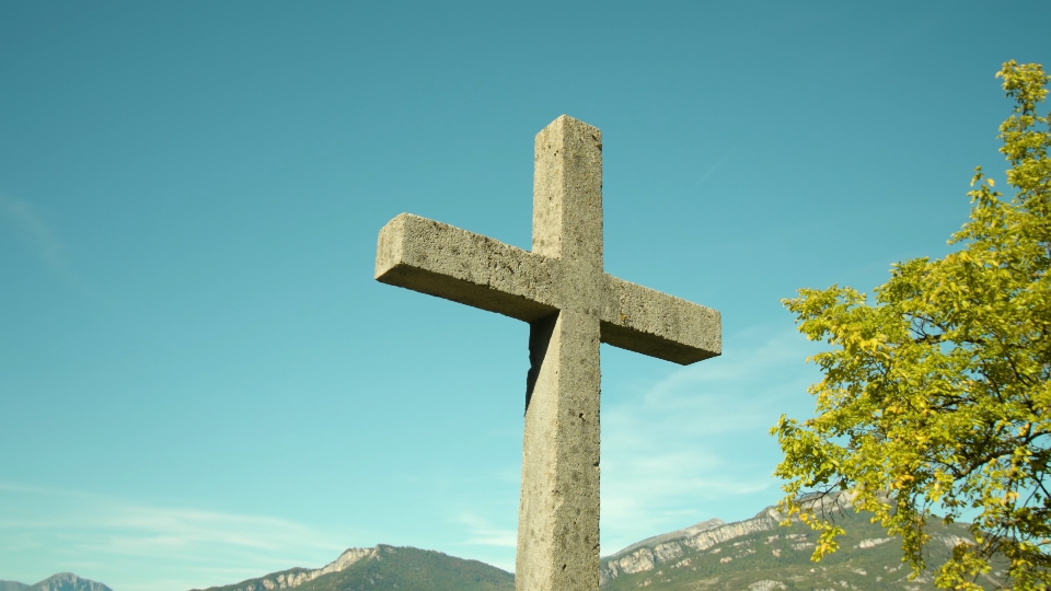Monumento a croce litica davanti montagne e alberi nel parco