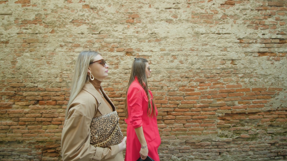 Women friends walk along shabby wall of Ventian building