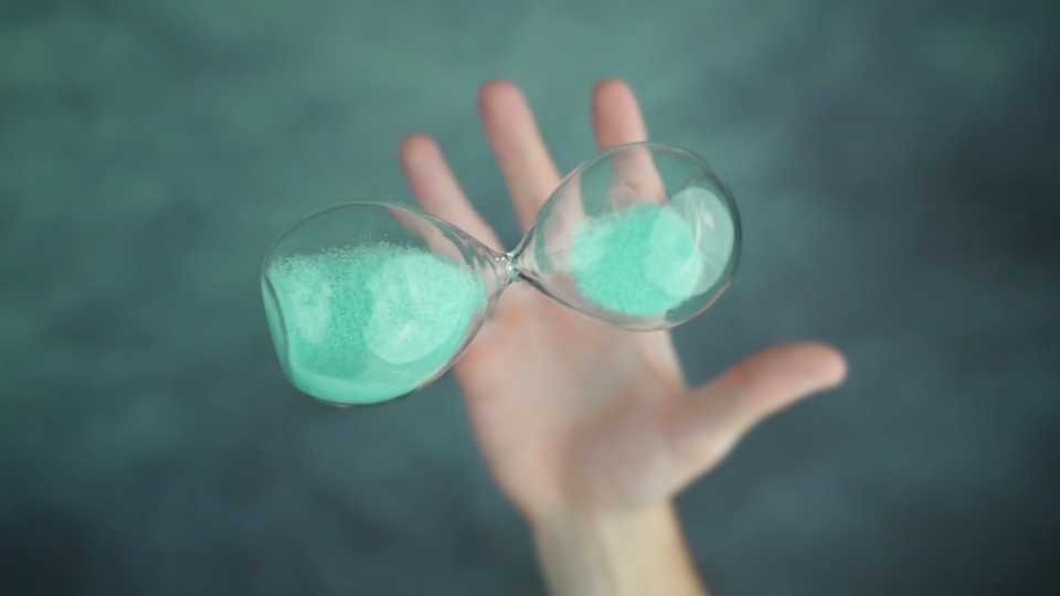 Person throws up and catches hourglass with bright sand