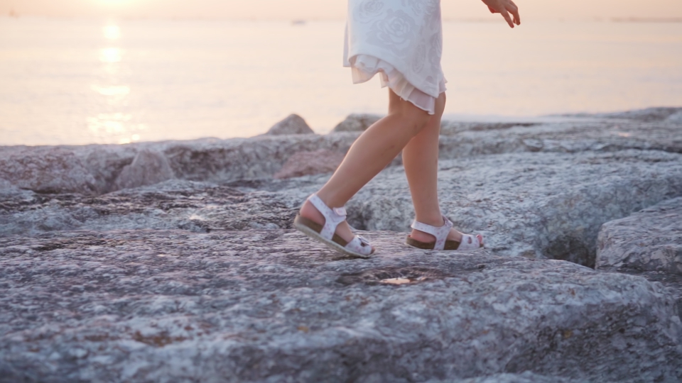 Little girl runs on the stones of the dike in slow motion