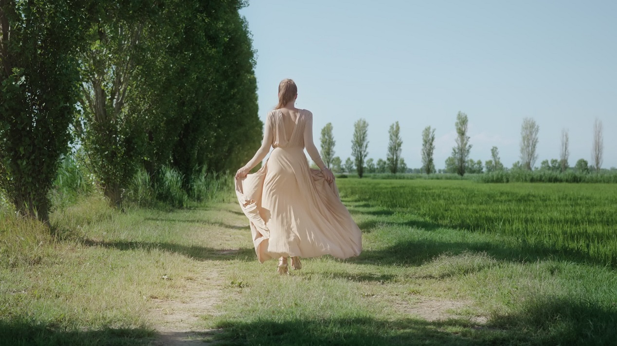 Eleganza nella Natura: Donna in Abito Cammina tra Campi Verdi