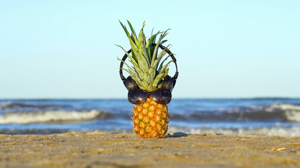 Ananas con occhiali e cuffie sulla sabbia del mare